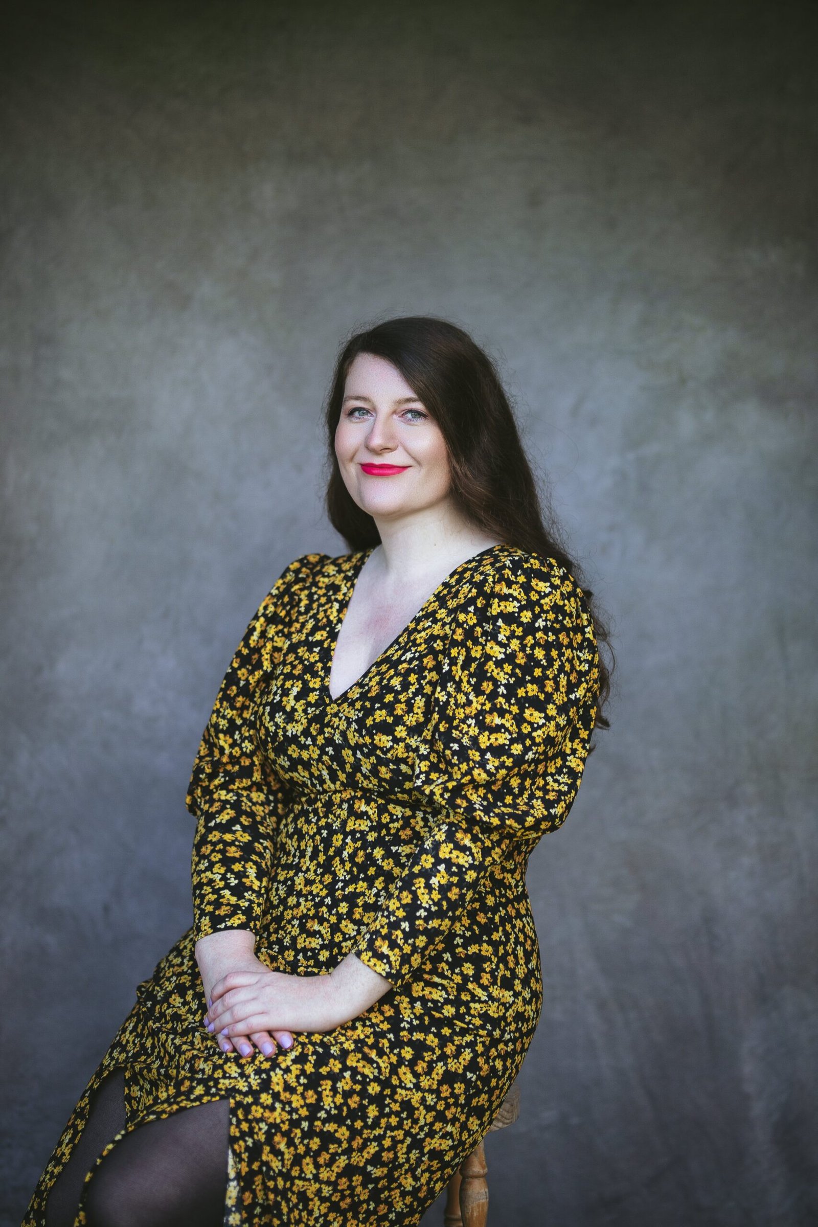 Rachel Thompson, sits wearing a dress with yellow florals and black background.